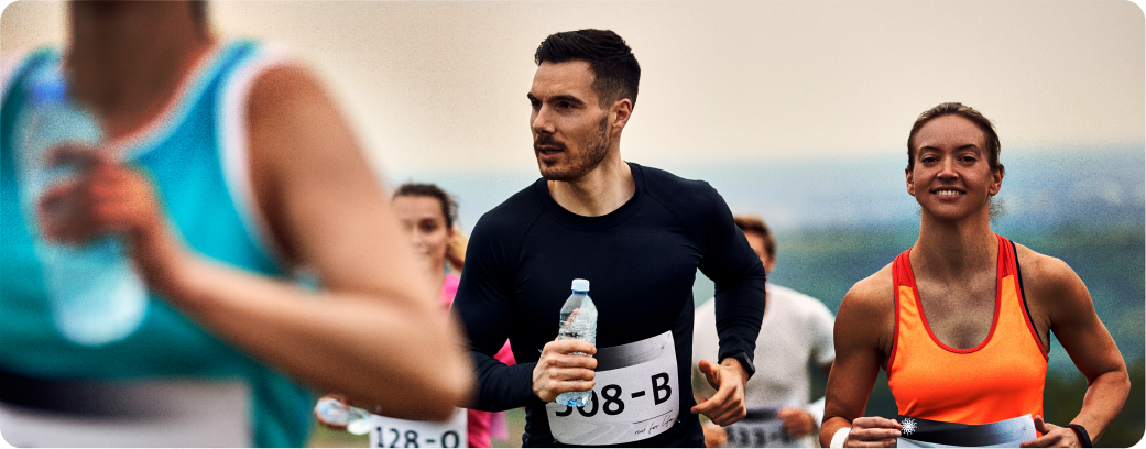 Homem e mulher correndo com outros participantes durante um evento esportivo ao ar livre.