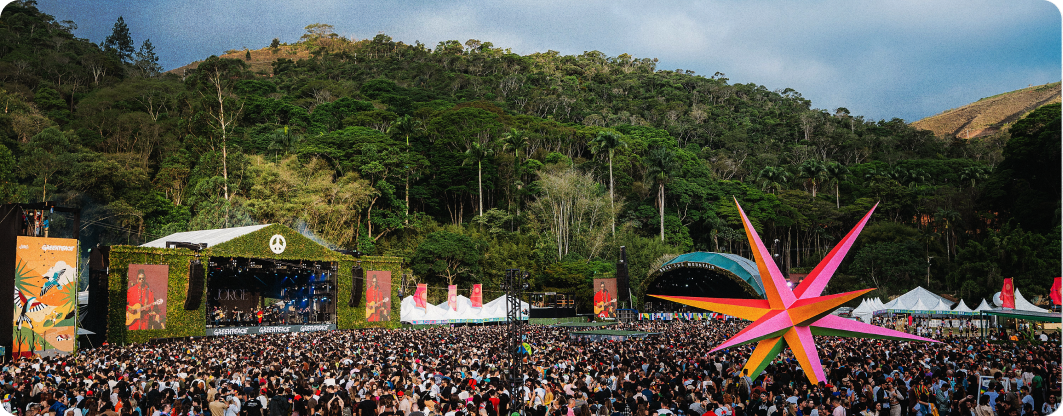 Vista aérea de um festival de música “Rock The Mountain”, com uma multidão de pessoas em frente a um palco principal.